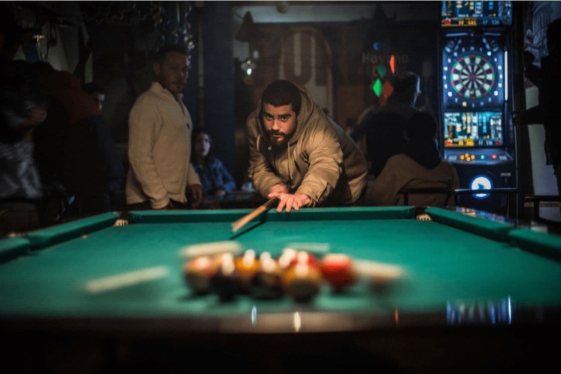 A guest lining up a pool shot in the Innisfree game room, with a dartboard machine behind him
