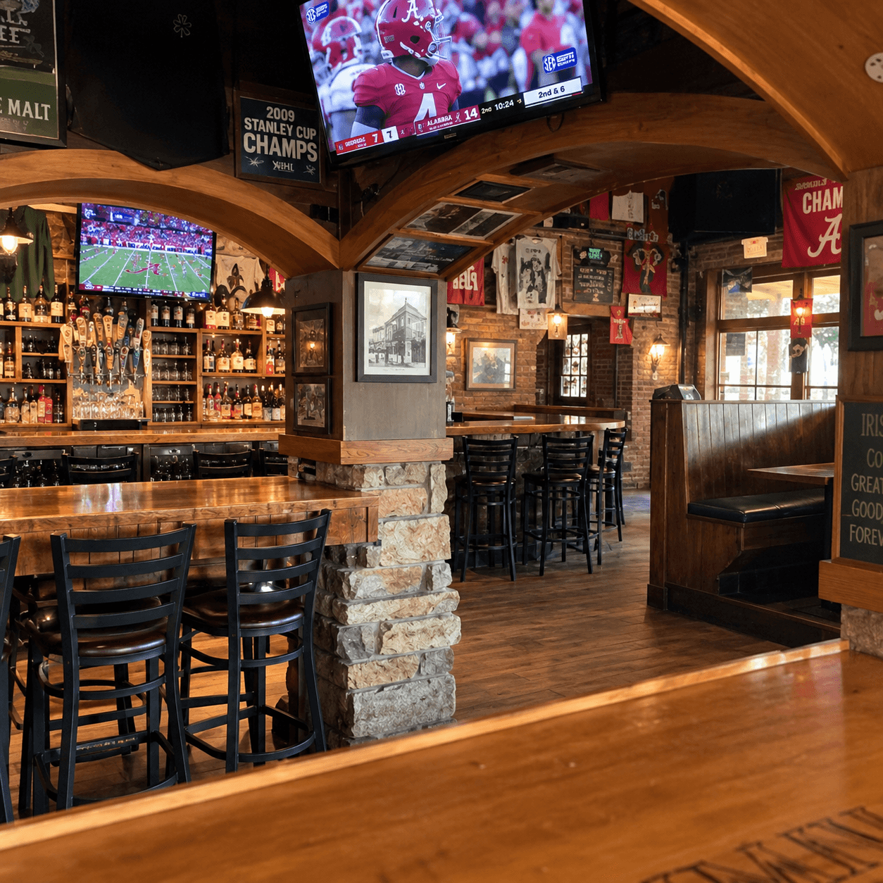 Inside Innisfree: the wood bar, draft taps and an Alabama football game on the TVs, with Crimson Tide banners on the brick walls